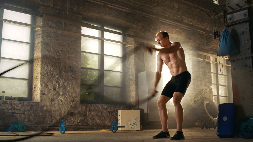 Muscular Shirtless Man in a Gym Exercises with Battle Ropes During His Cross Fitness Workout  High-Intensity Interval Training.