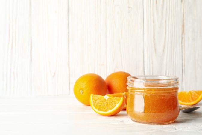 Oranges, spoon and glass jar with jam on wooden background