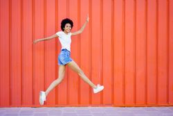 Side view of woman happily skipping in front of red wall