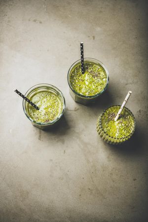 Three green smoothies in glasses with eco friendly straws on concrete background, copy space