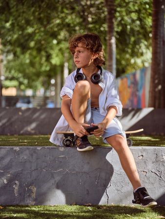 Child sitting on skateboard in park and looking away