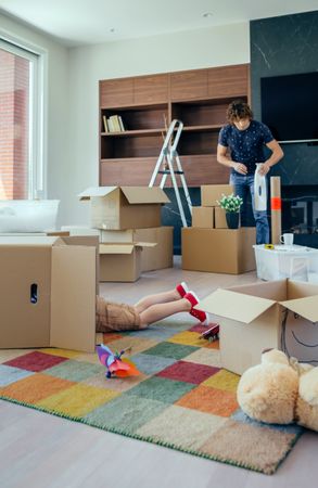Boy playing inside a moving box while his father unpacks