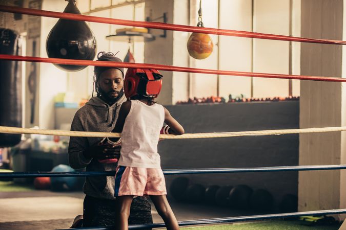 Rear view of a boxing student talking to her coach standing inside the boxing ring
