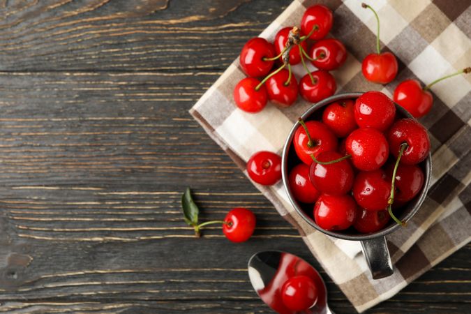 Towel and metal mug with cherry on wooden background, top view