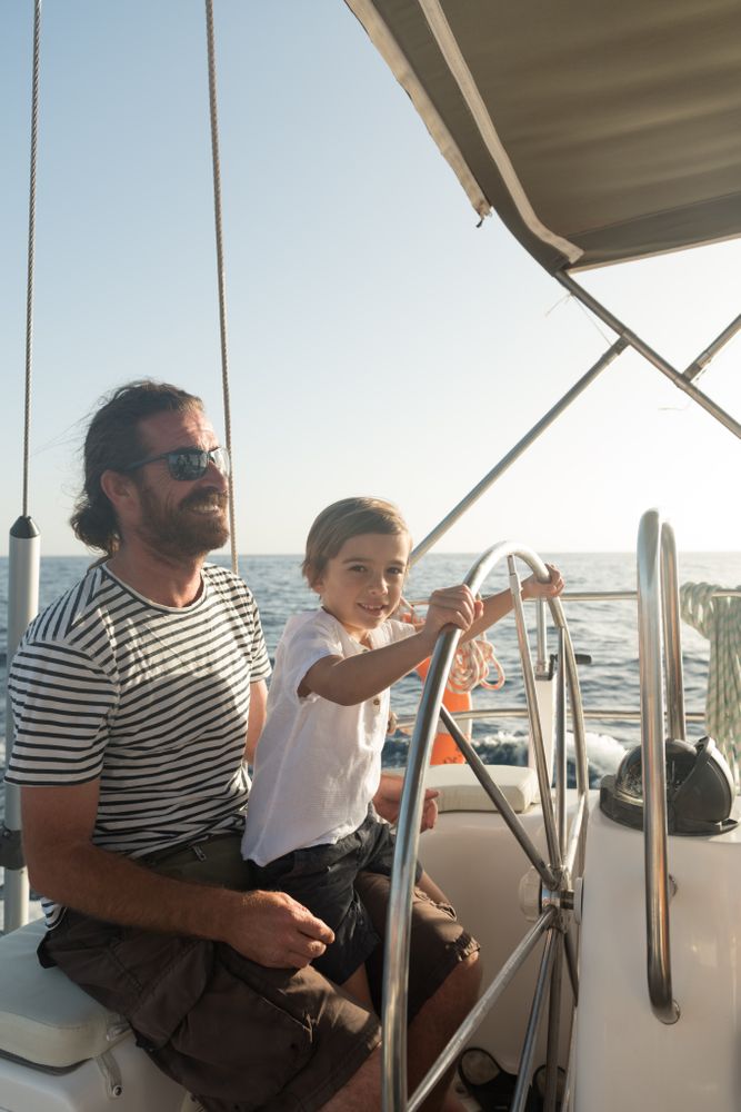 Man and boy holding steering wheel on yacht on water