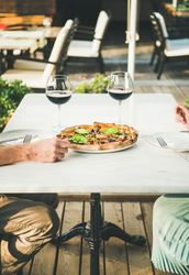Couple sitting outside with red wine and a freshly made pizza in between them