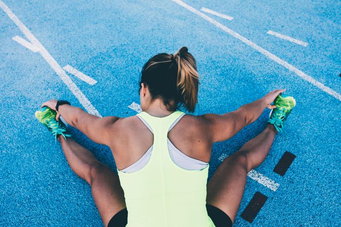 Young woman sitting on a track field stretching her legs