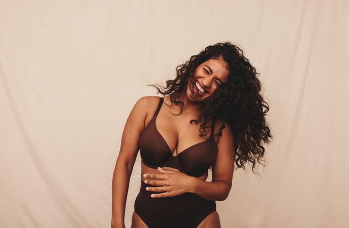 Happy young woman laughing with her eyes closed in a studio background in brown undergarments