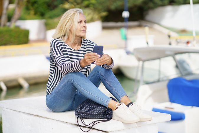 Older woman using her smartphone sitting in a sea port