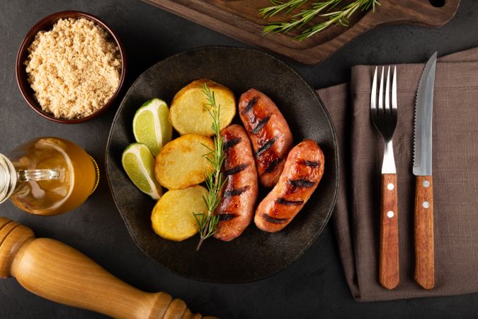 Top view of grilled sausages served with potatoes, lime and rosemary garnish