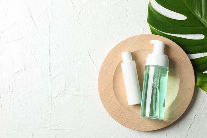 Palm leaf, wood plate, bottles with scrub and cream on neutral background, copy space