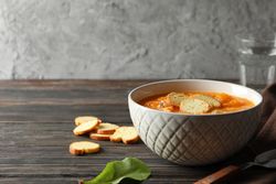 Bowl of delicious pumpkin soup on table with glass of water with copy space