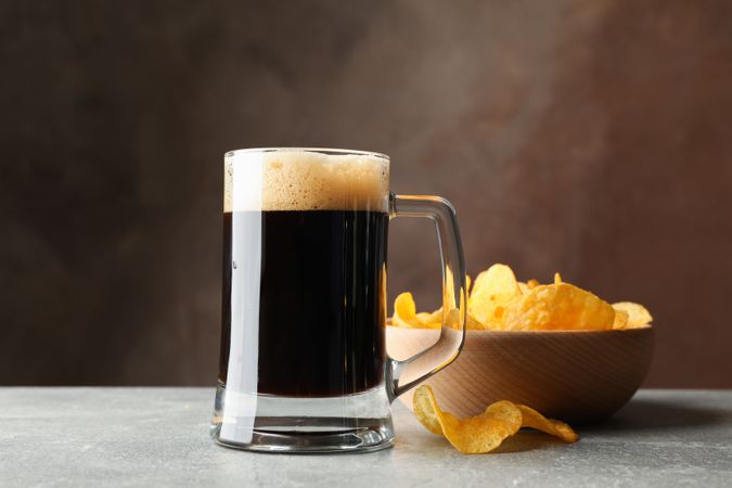 Glass of dark beer and chips on grey table, space for text