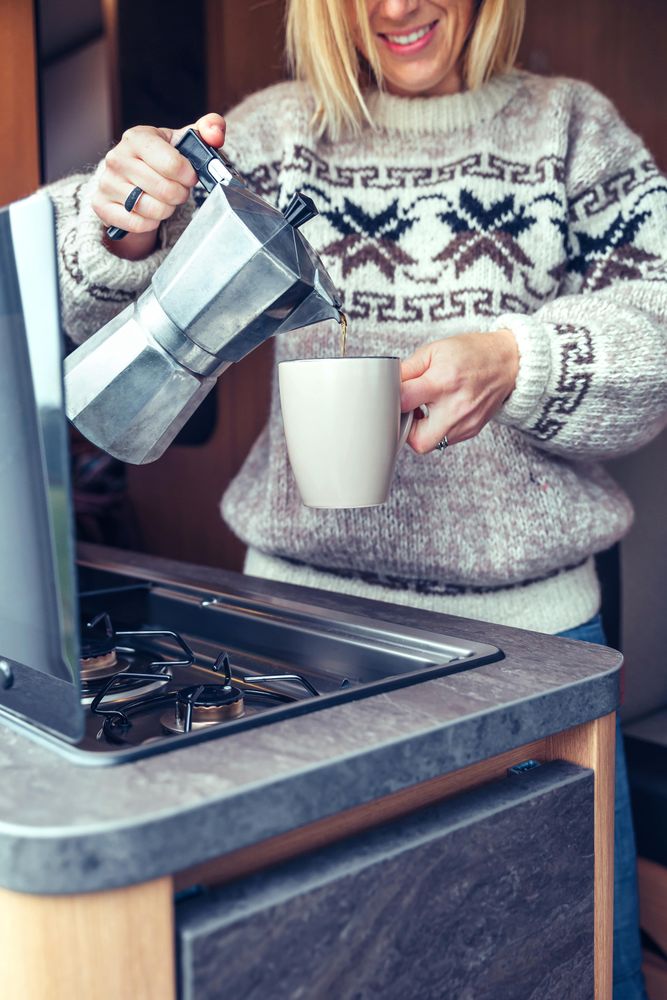Women in warm sweater pouring coffee from moka in back of van, vertical close up
