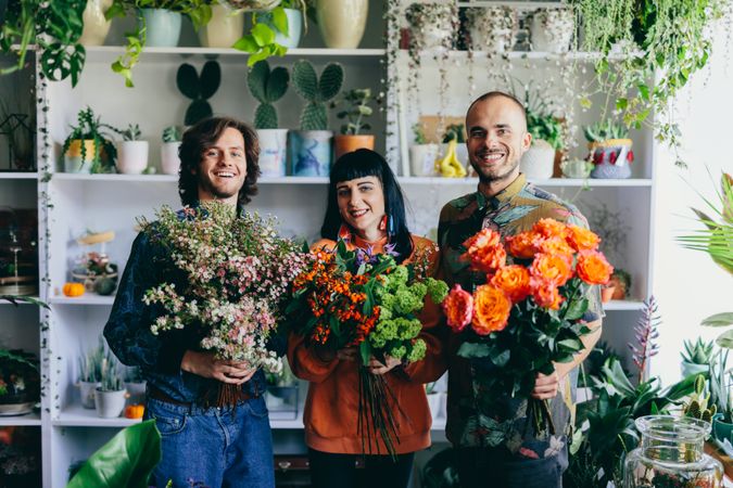 Woman and two men holding flowers in the flower shop.