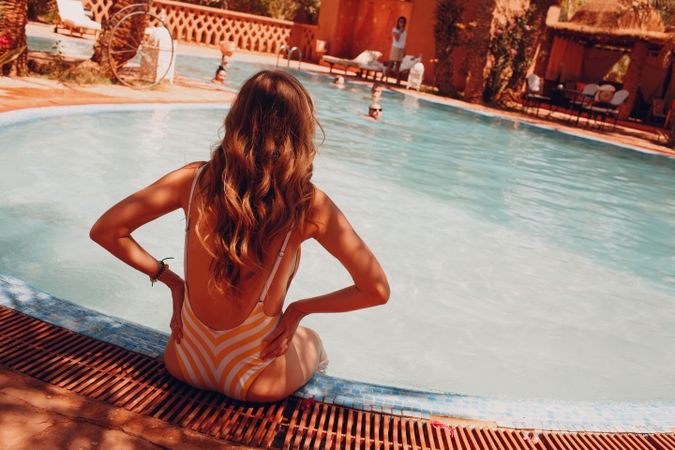 Back view of woman in brown bikini sitting on swimming pool side