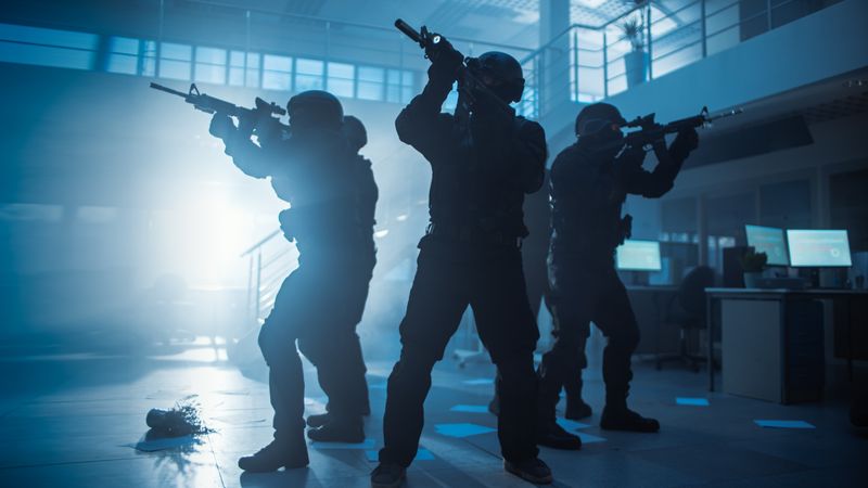 Masked Squad of Armed SWAT Police Officers in a Hall of a Dark Seized Office Building with Desks and Computers.