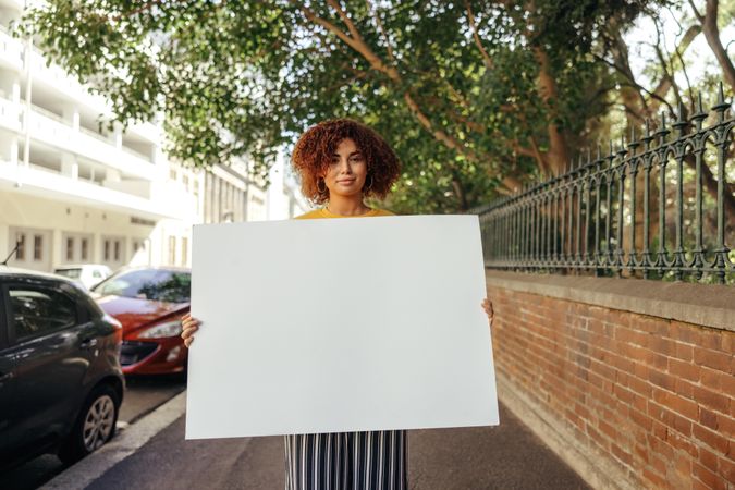 Confident young woman holding a blank placard in the city