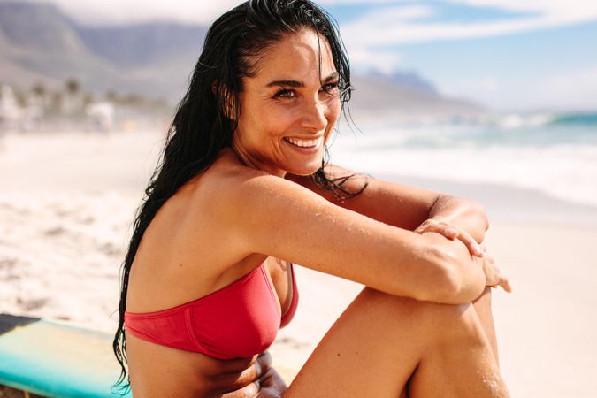 Cheerful woman in bikini sitting on beach