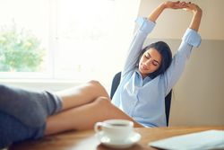 Woman at her office desk stretching her arms up with feet on desk