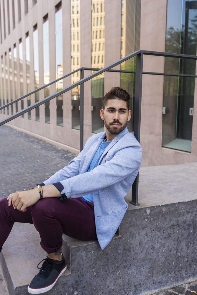 Portrait of happy bearded young man sitting on steps outside