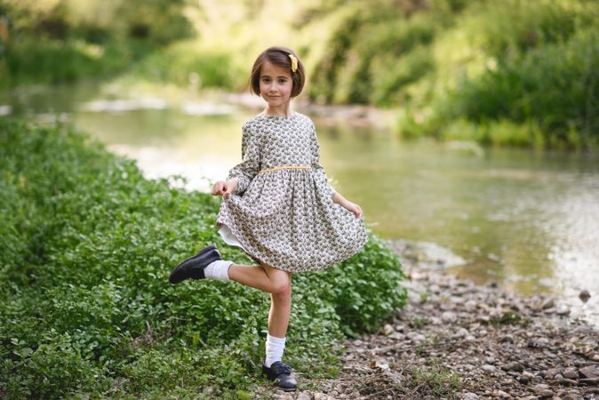 Child in dress curtsy with her dress next to river