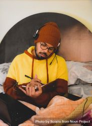 Man in yellow hoodie using smartphone writing notes and using laptop in bed 5RBqW5