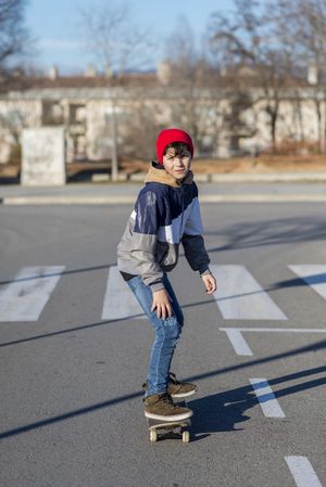 Teenage skateboarder riding on street in front of cross walk