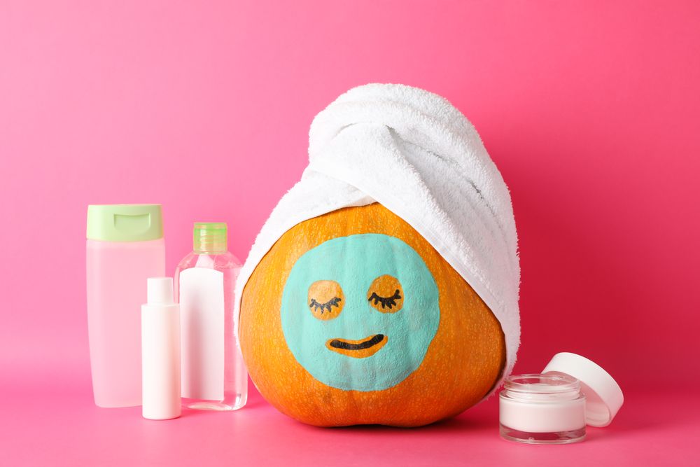 Funny pumpkin and skin care accessories on pink background, space for text