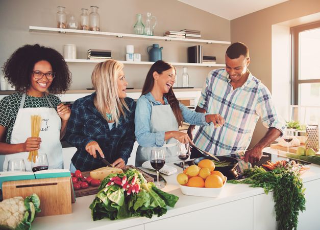 Friends joking together while cooking dinner in a bright kitchen with red wine