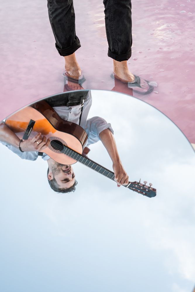 Reflection of inspired musician playing guitar at seashore in mirror