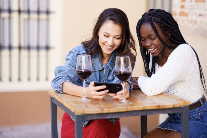 Female friends smiling at phone screen at a restaurant with red wine