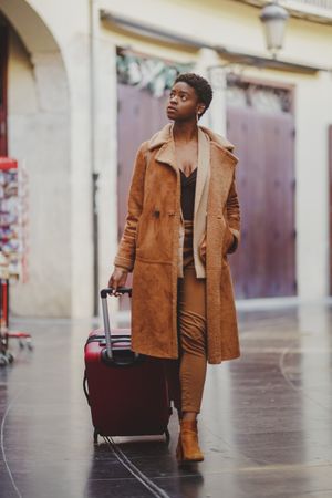 Stylish Black woman with luggage walking on street