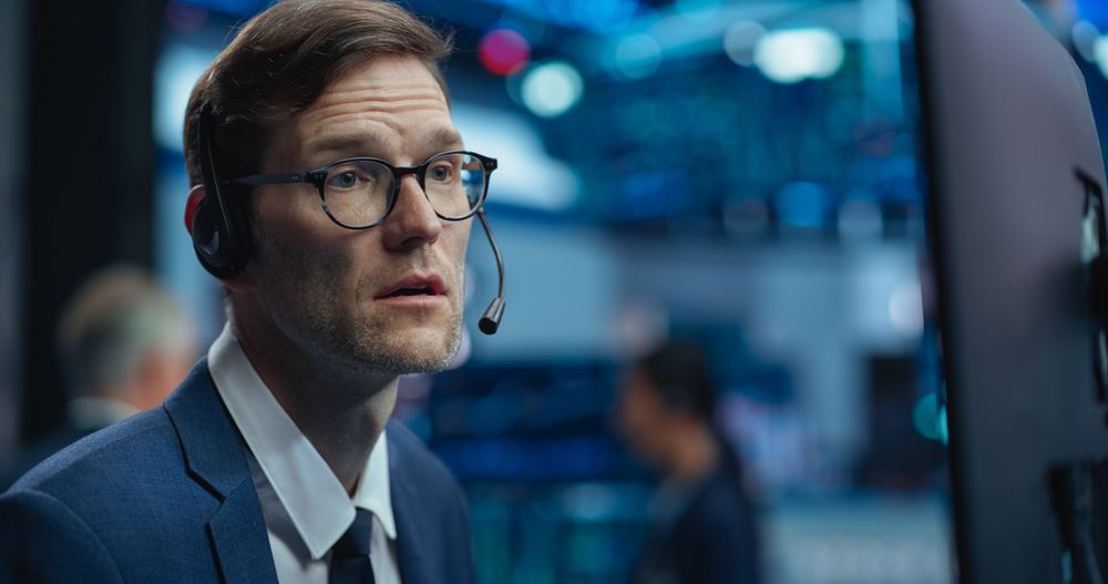 Adult Man in Glasses Looking at Computer Screen, Communicating with a Client on a Phone Call, Talking About a Buying Strategy
