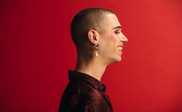 Profile view of man wearing an earring and makeup smiling