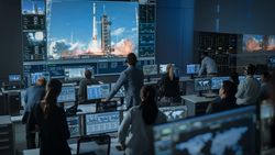 Diverse Team in Mission Control Observes Rocket Launch on Giant Screen.
