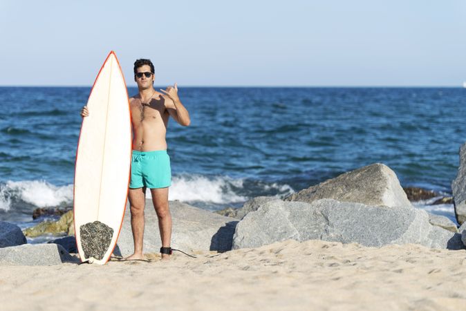 Male surfer standing with red outlined board on rocky coast