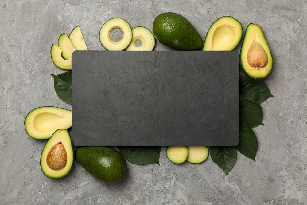 Avocado, leaves and board with space for text on gray background