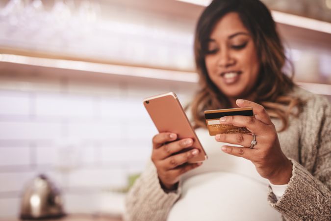 Smiling pregnant woman shopping on smart phone using credit card for payment
