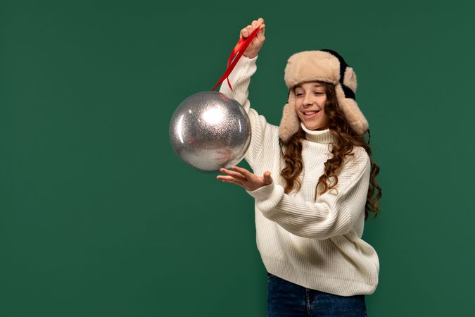 Smiling girl in fur hat holding large silver ornament