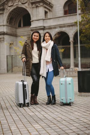 Two smiling Asian tourist women with suitcases