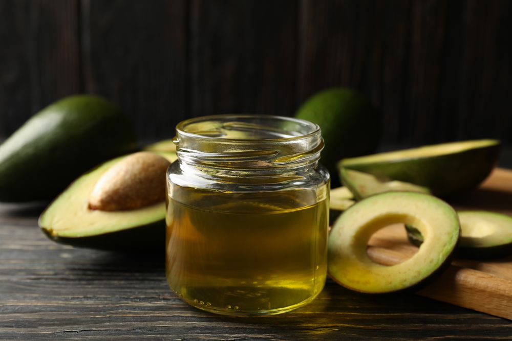 Board, avocado and oil on wooden background, close up