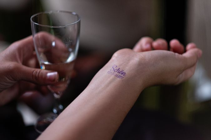 Person holding alcoholic drink and looking at their stamped wrist