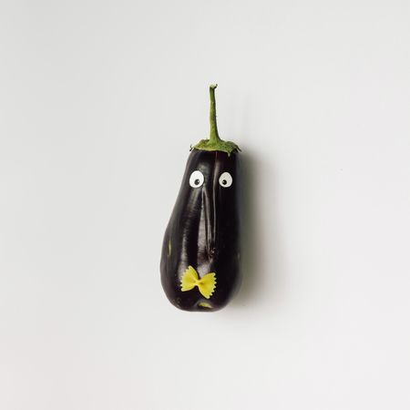 Eggplant with googly eyes and bowtie pasta on light background