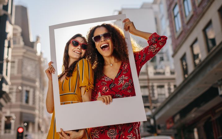 Friends standing in the city holding an empty photo frame