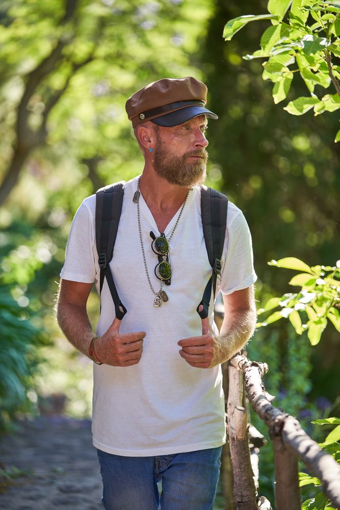 Traveling bearded man in cap walking in forest