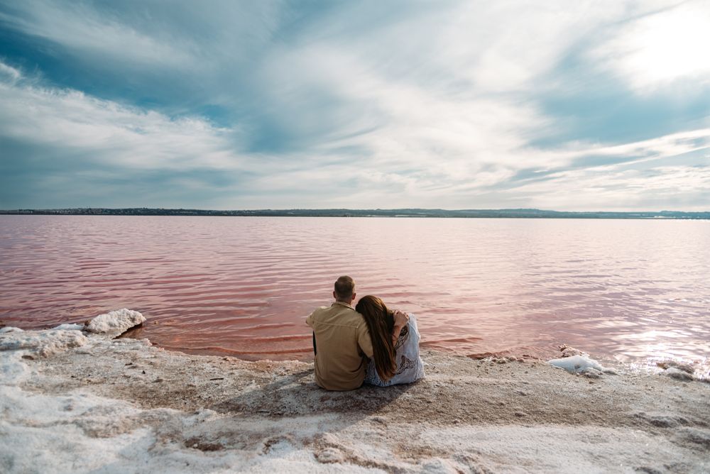 adorable couple sitting on an amazing beach with pink water