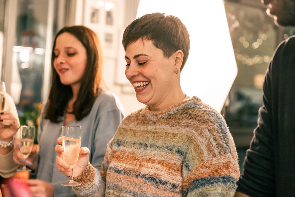 A young woman laughing with joy while holding a glass of champagne at a party.