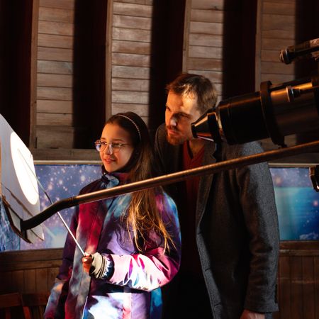 Mentor and student observe projected solar image through telescope.
