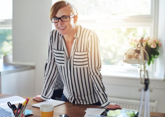 Smiling female entrepreneur leaning on her desk in bright office